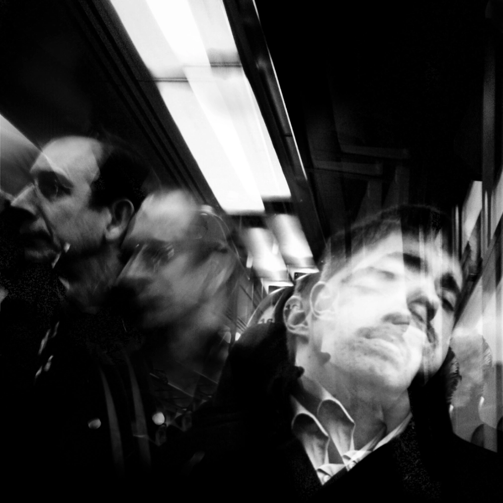 multiple-exposure photograph of a man asleep on a train seat, his head tilted back, with repeated ghosted positions of his head as well as the passenger to his left.