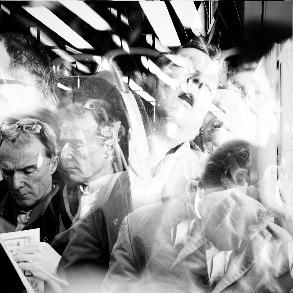 Black-and-white multiple-exposure image inside a train carriage showing two different men seated: one on the left reading a newspaper and another on the right asleep with his head tilted back.
