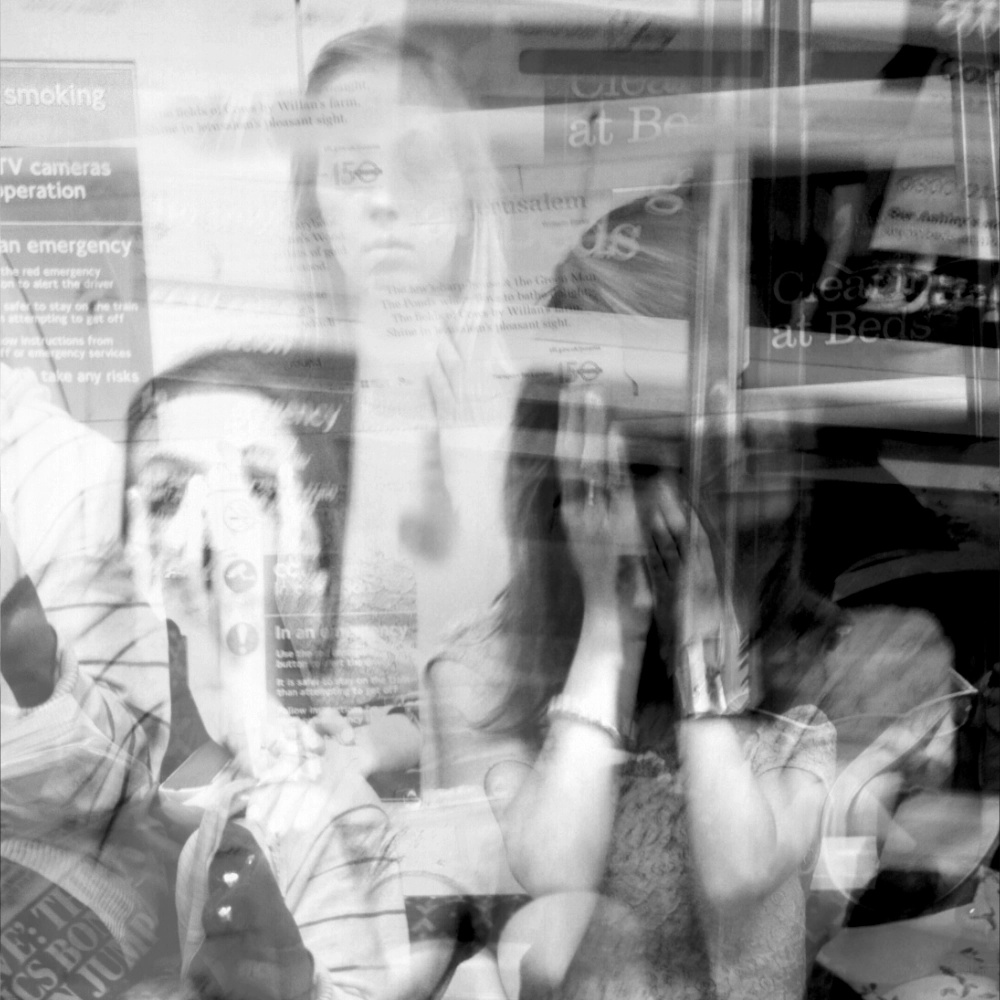 Black-and-white multiple-exposure photograph of a woman sitting on a train seat; overlapping exposures show her with her hands raised near her face in slightly different positions, creating layered views of her face and arms against the carriage interior.