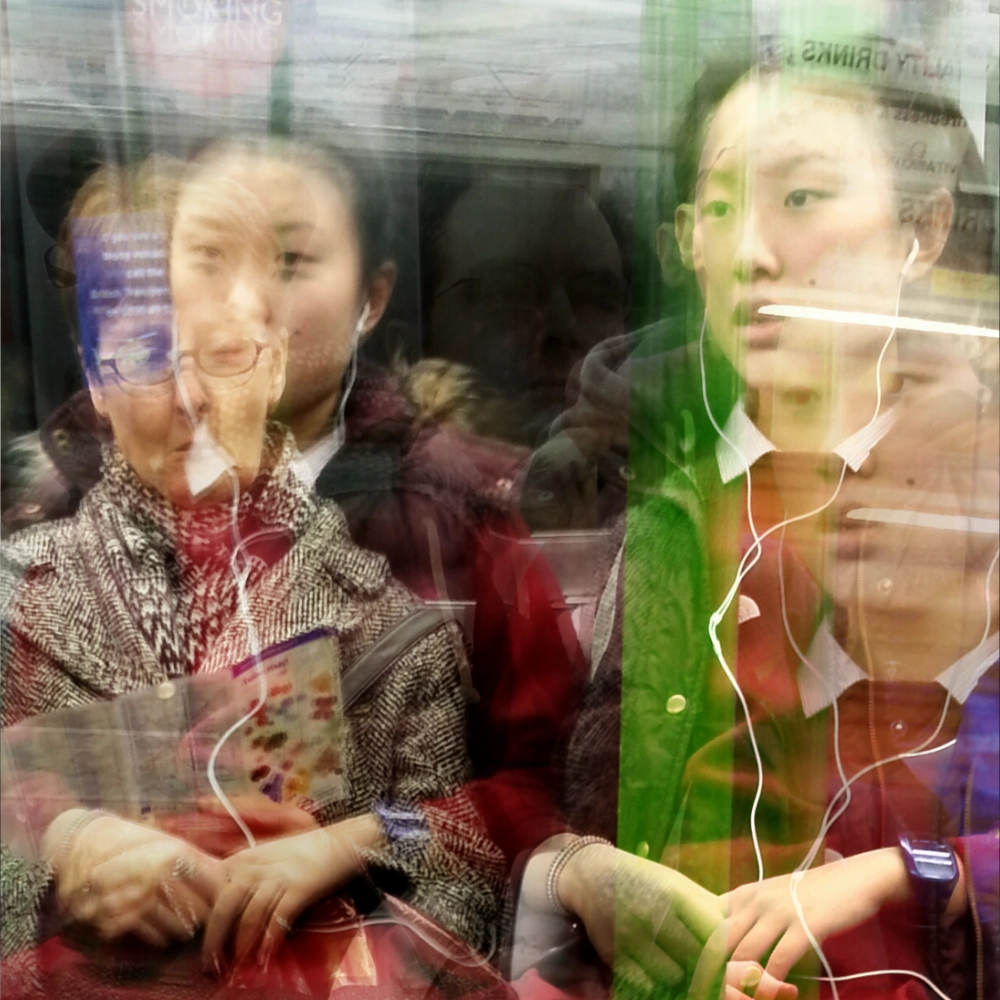 A multiple‑exposure photograph on a subway carriage, showing a girl repeated several times. One of her exposures overlaps with an older woman in glasses and a wool coat, with a colourful printed item visible in another layer.