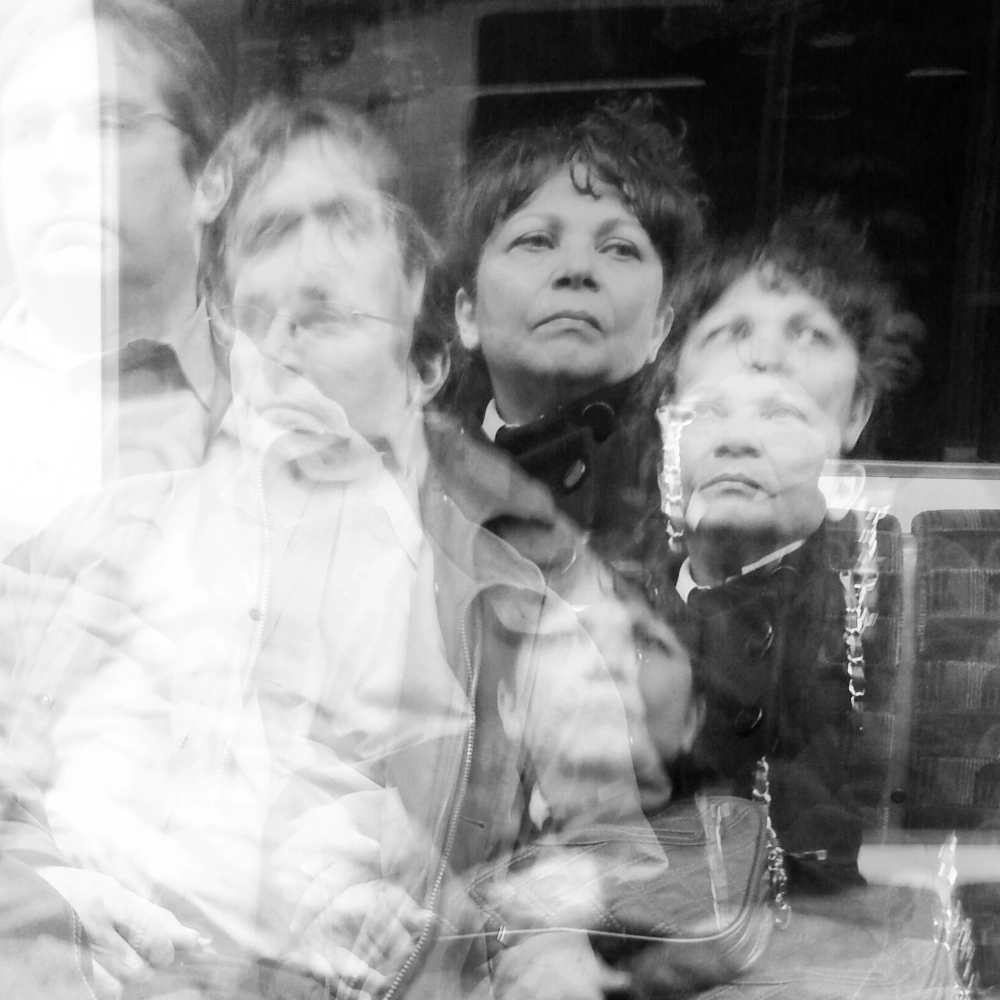 A multiple‑exposure photograph on a subway carriage, showing overlapping images of two people seated together, their faces, jackets, and upper bodies layered in several offset positions against the patterned bench. If you’re planning to harmonise the full set for length or rhythm, what character range are you leaning toward for the final sequence?