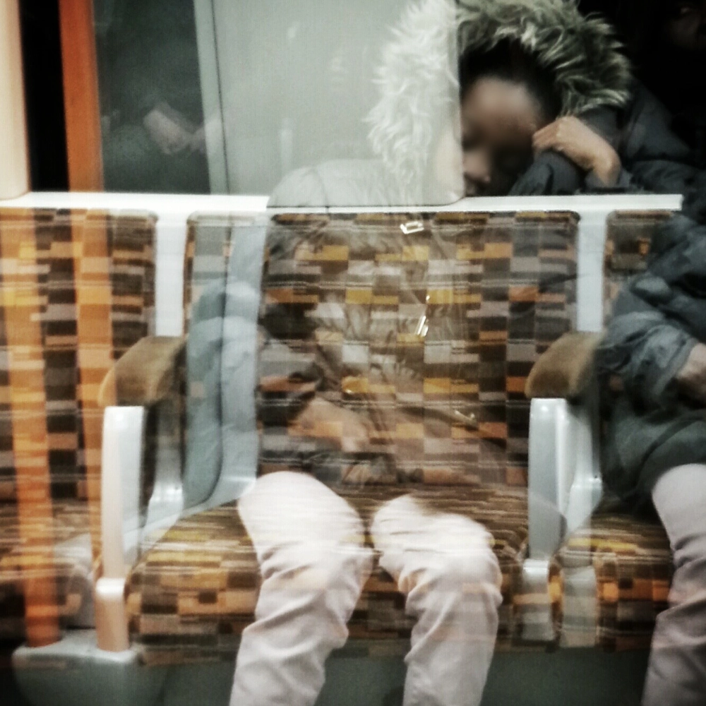 A multiple‑exposure photograph on a subway carriage, showing overlapping images of a sleepy child in a fur‑trimmed hooded coat seated on a patterned bench.
