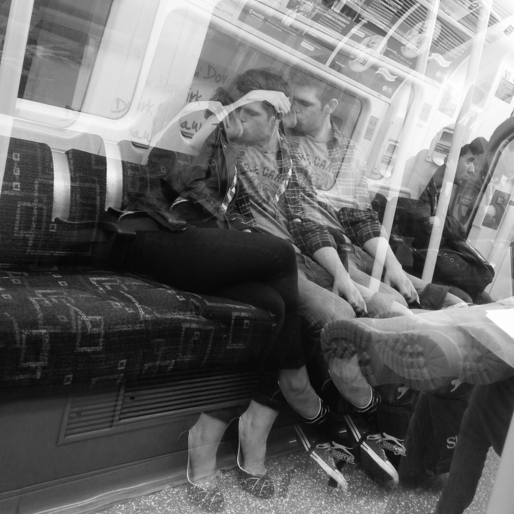 A multiple‑exposure photograph on a subway carriage, showing overlapping images of two people seated close together and kissing.