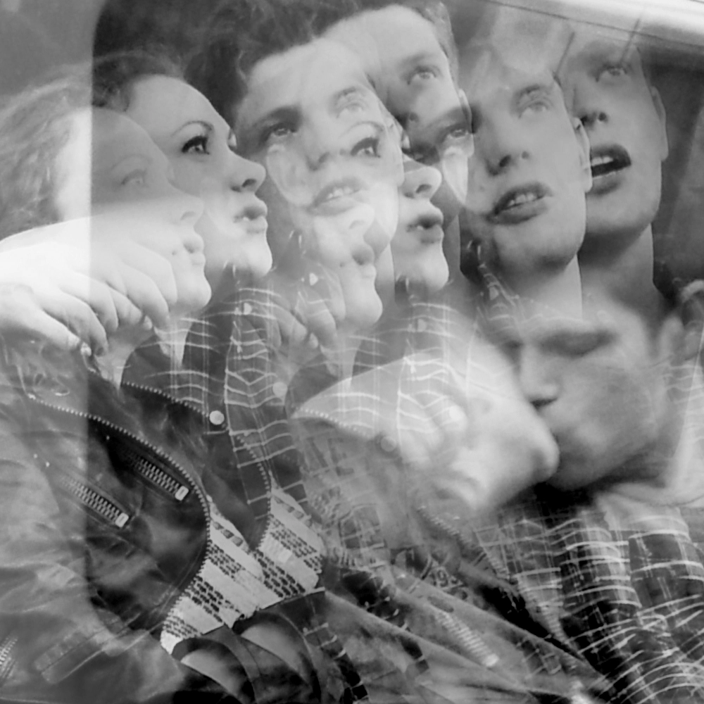 A multiple‑exposure photograph on a subway carriage, showing overlapping images of two people seated together, their faces, shirts, and leaning postures layered in several offset positions, including one position where they are kissing.