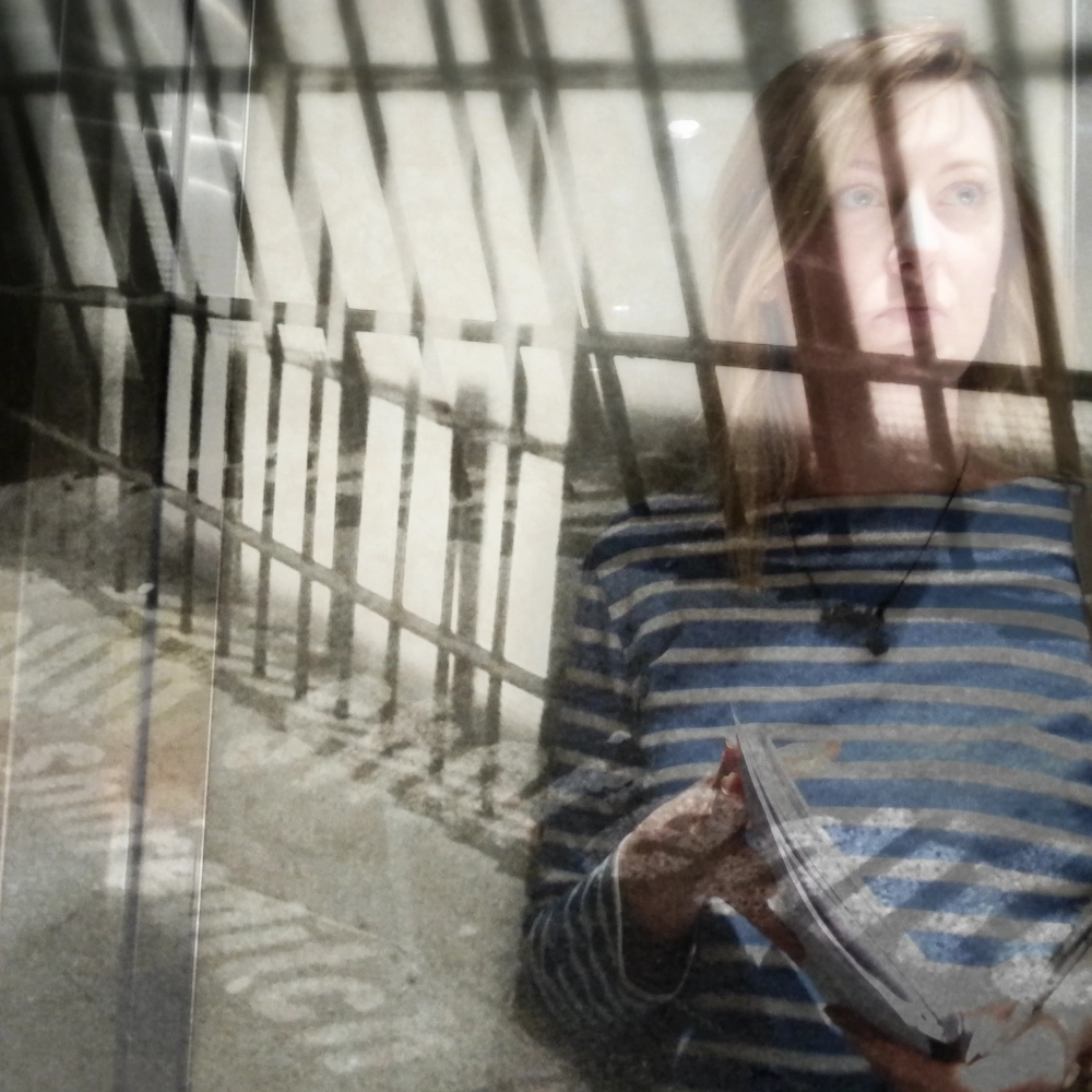 A multiple‑exposure photograph showing overlapping images of a person in a striped shirt holding papers, their face and upper body layered in several offset positions against a set of vertical bars, with the word “Shoreditch” repeated in the lower left of the frame.